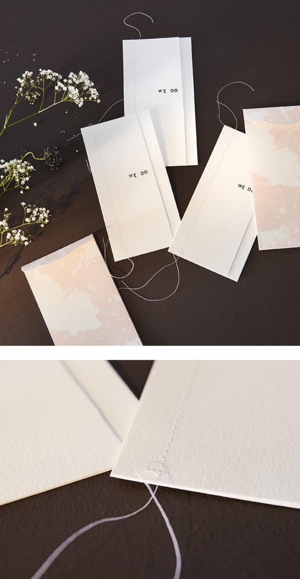 Invitations blanches pour un mariage, personnalisées avec des tampons et une couture en fil.