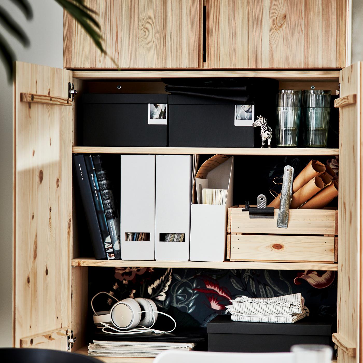 IVAR shelving unit with the bottom two doors open revealing household items such as magazine files, boxes, and headphones.