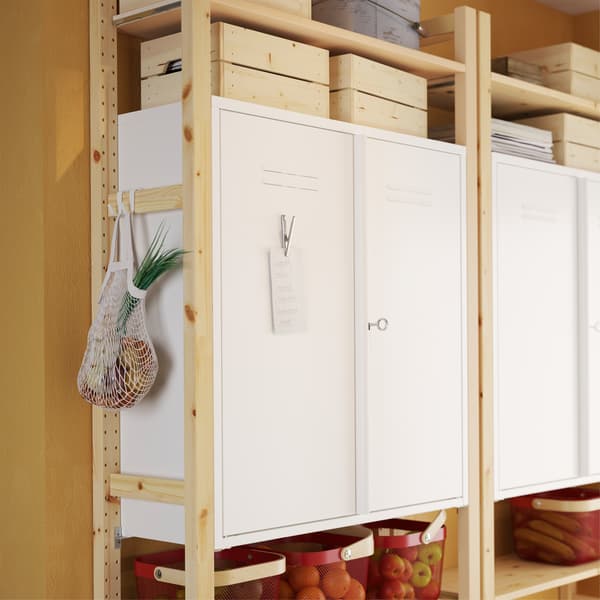 IVAR white metal cabinets on shelf sections in pine and a metal clip with a note is placed on the metal door of the cabinet.
