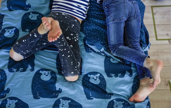 Jambes de deux garçons couchés sur un lit revêtu d’une couette bleue décorée de motifs d’animaux.