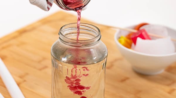 Jemand füllt flüssiges Wachs in ein Glas mit heißem Wasser