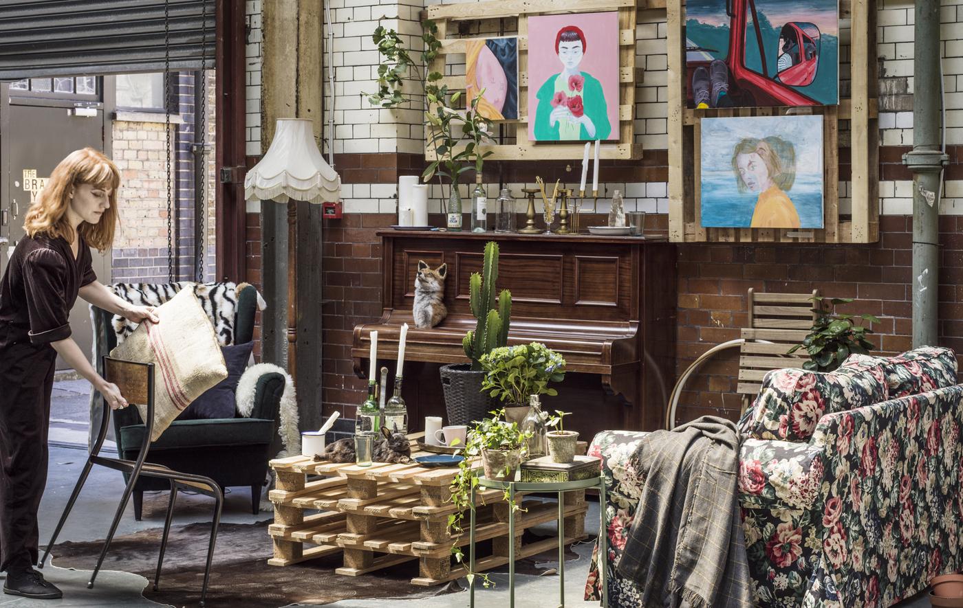 Jeune femme dans un salon commun, équipé de meubles de styles variés et de plantes.