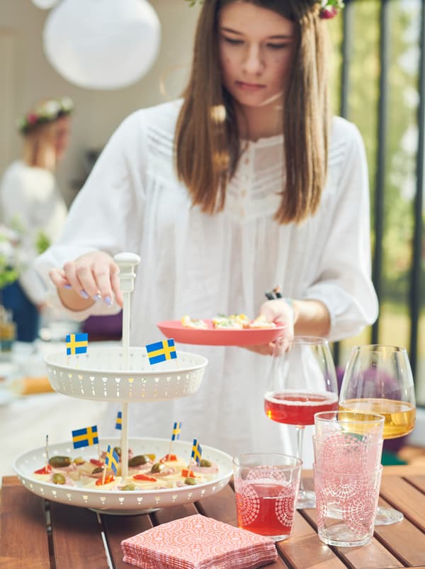 Jeune femme se servant d’amuse-gueule sur un présentoir GARNERA posé sur une table à côté de verres DYRGRIP remplis d’une boisson.