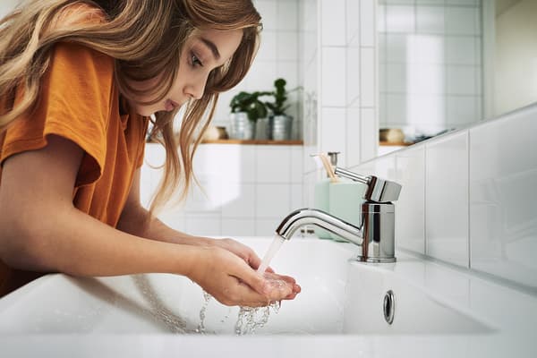 Jeune fille attrapant l’eau qui coule du robinet avec ses mains.