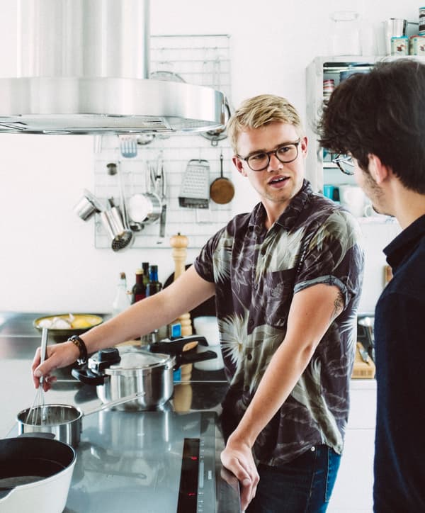 Jeune homme en train de fouetter dans une casserole posée sur une cuisinière, dans une cuisine moderne.