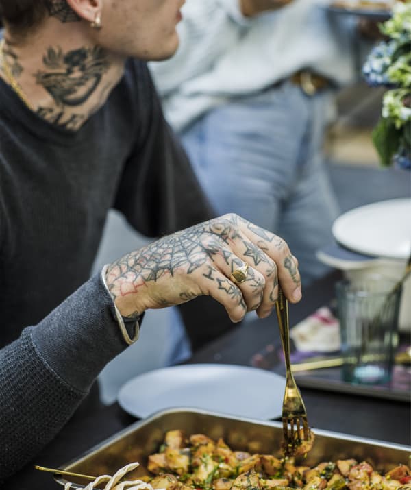 Jeune homme tatoué tenant une fourchette au-dessus d’un plat de service