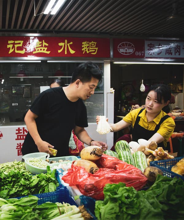 Jiaqin stands at a vegetable stall.