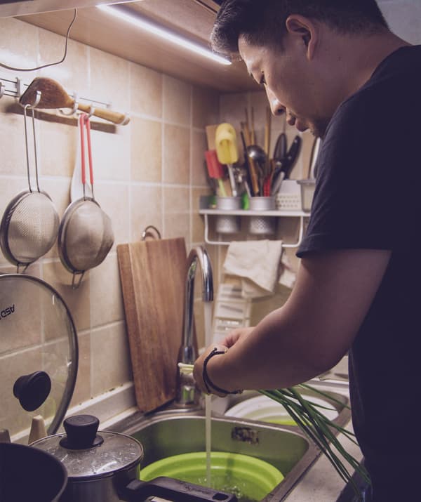 Jiaqin washes vegetables in the kitchen sink.