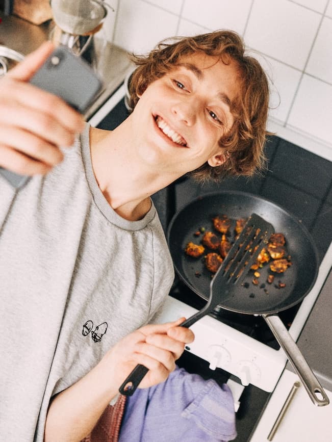 Joven sosteniendo un celular en su mano, tomando una foto a un sartén con comida dentro de el.
