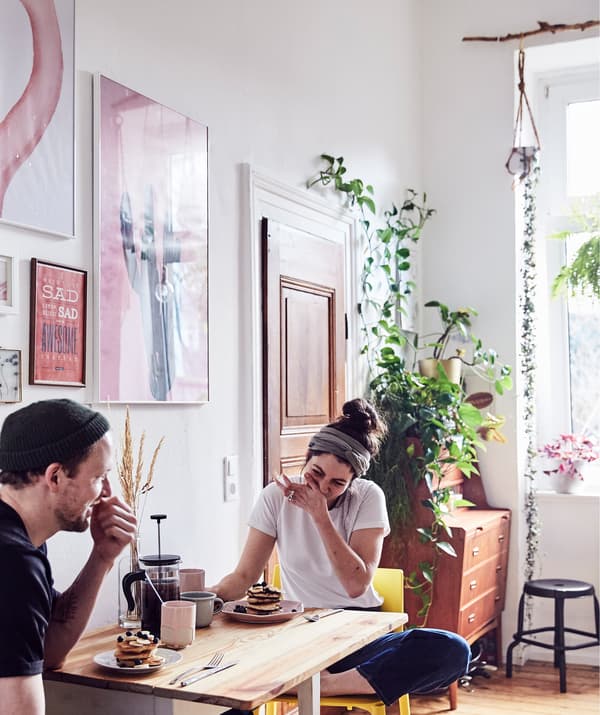 Julia and André eating breakfast at a drop-leaf table in a room with plants and artwork on the walls.