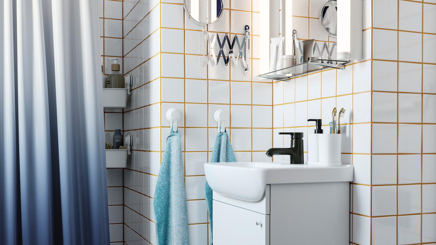 Kabinet sink cuci tangan berwarna putih, paip berwarna hitam, jubin berwarna putih dengan turap berwarna kuning, tirai bilik mandi berwarna biru gelap, pencangkuk dengan tuala.