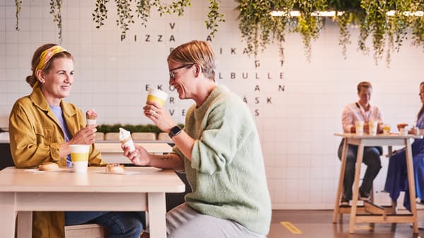 カフェで2人がテーブルに座り、アイスクリームとドリンクを楽しんでいる。背景に緑の装飾。