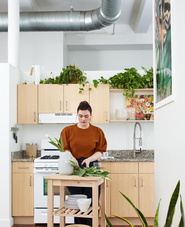 Kara arranging flowers in a vase on a wooden trolley in the kitchen.