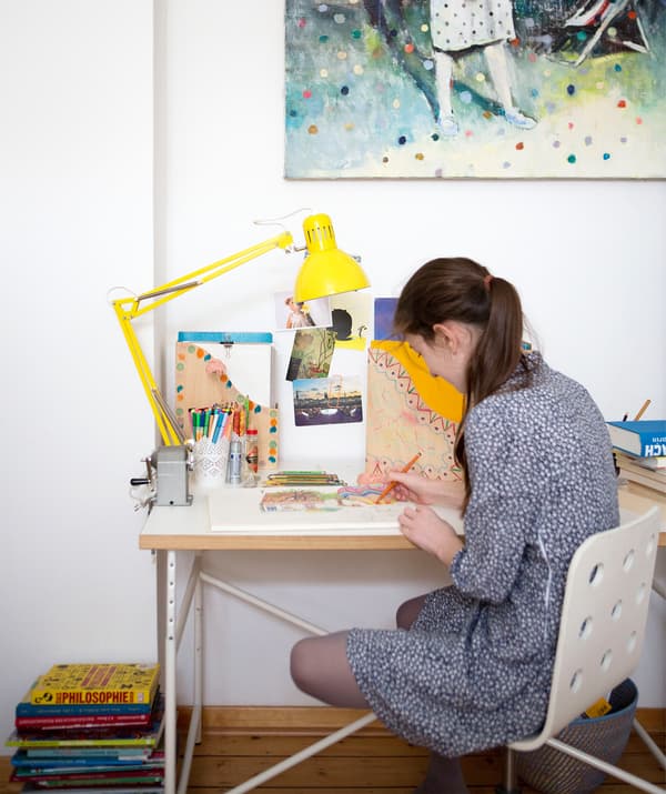 Karlotta drawing at her desk with yellow desk lamp and box files.