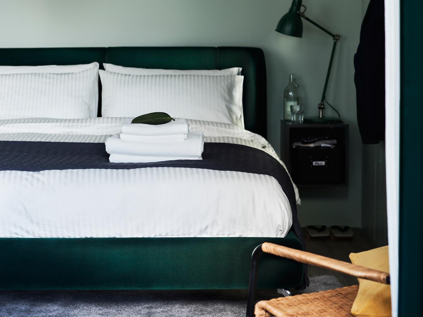 Katil upholsteri TUFJORD berwarna hijau gelap dengan linen katil NATTJASMIN terletak bersandar pada dinding berwarna hijau di dalam bilik tidur.