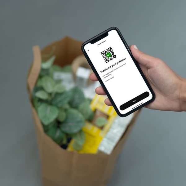 Keca puna sa IKEA proizvodima položena na podu. Ruka koja drži teledon na kojem je otvorena opcija IKEA Scan u okviru IKEA aplikacije
