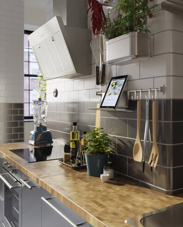 Keuken in roestvrij staal, een houten werkblad, verse kruiden en een wandgemonteerde stang met een tablet op een tablethouder.