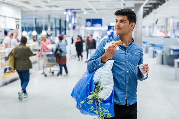Kille som bär på en blå shoppingkasse och håller en korv med bröd i ena handen.