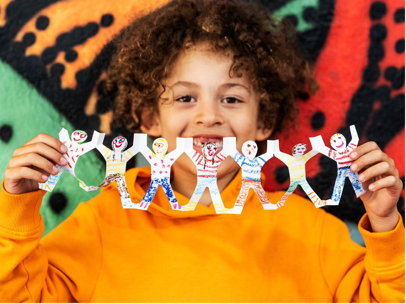 Kind houdt een kleurrijke papieren slinger met getekende figuurtjes vast, tegen een levendige achtergrond met graffiti.