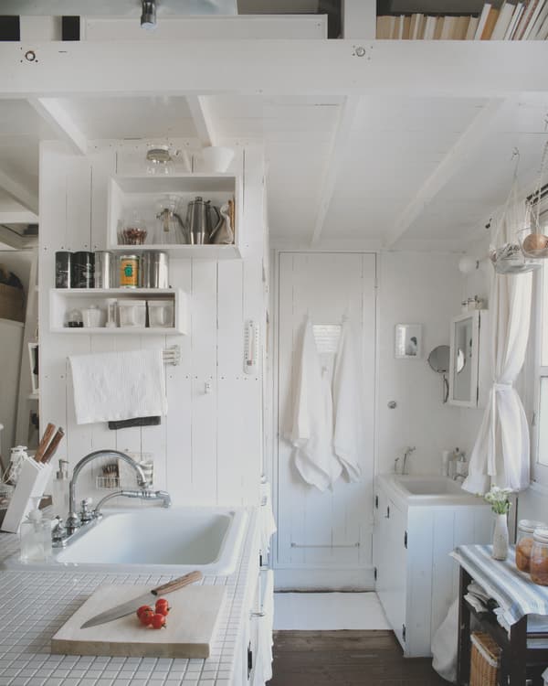 Kitchen storage and a tidy bathroom sink area in a small, white, Tokyo home.