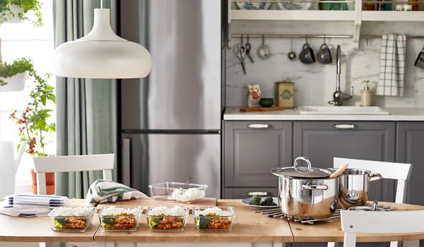 Kitchen table where batch-cooked, identical meals have been portioned from big pots into a row of glass food containers.