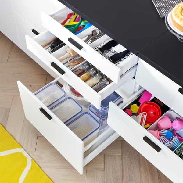 Kitchen with open drawers in white that display plastic food containers, kitchen utensils and colourful kitchen tools inside.