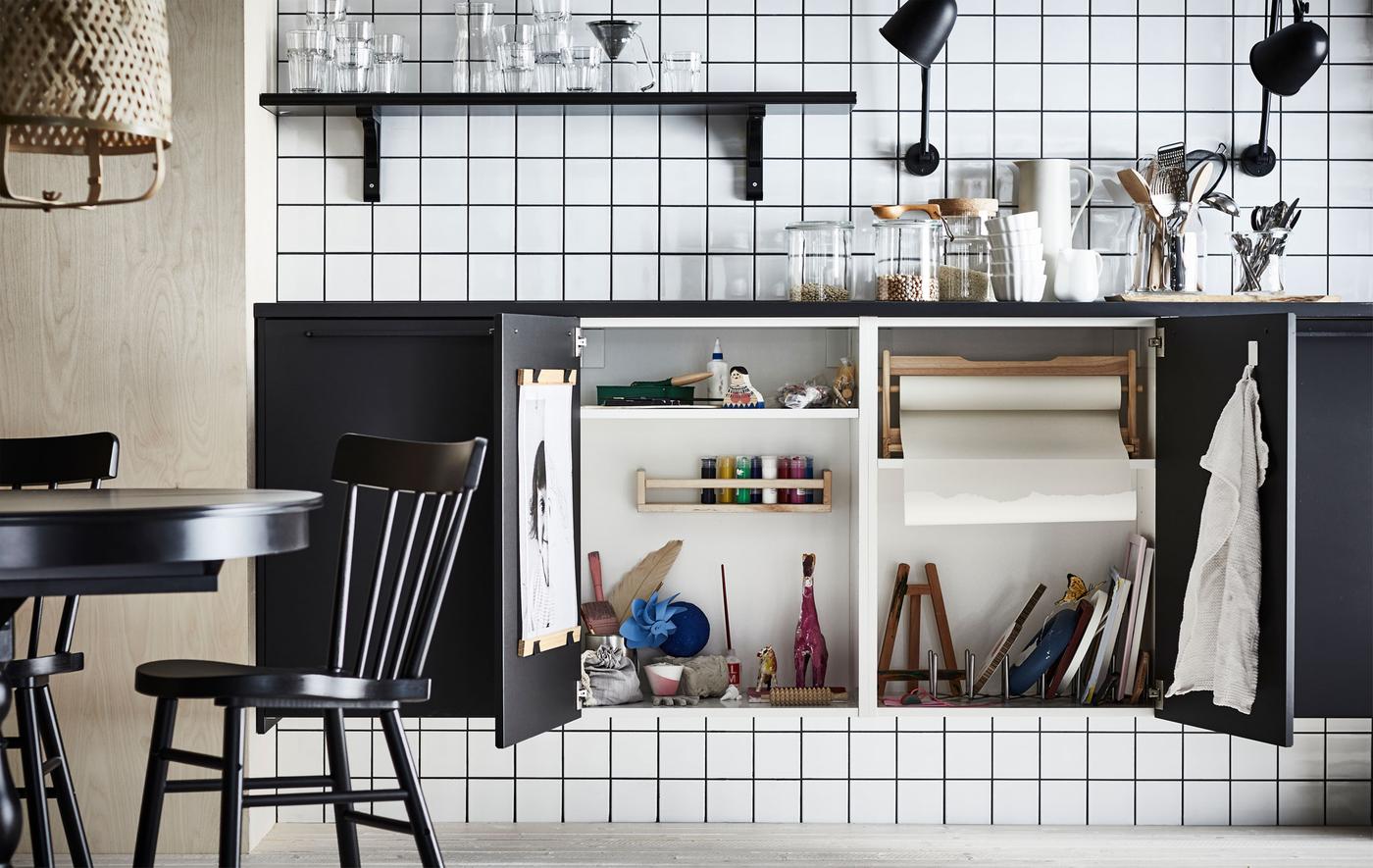 Kitchen worktop with two cupboard doors beneath swung open, revealing a complete miniature art studio hidden within.