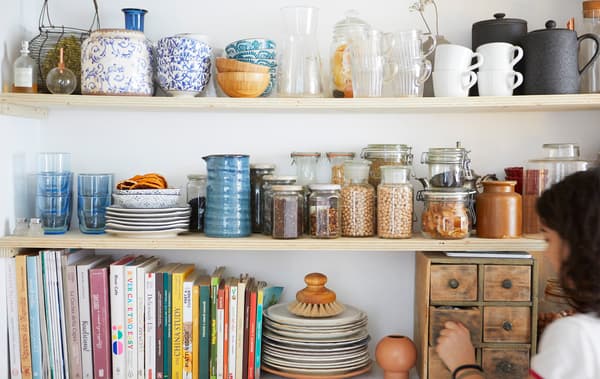 Kitchenware, books and jars of dry ingredients on three wooden shelves.