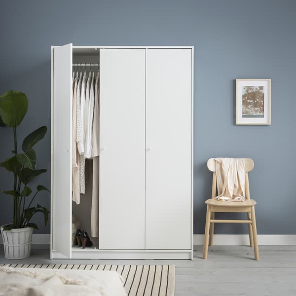 KLEPPSTAD wardrobe in white with hinged doors showing clothes hanging neatly from the clothes rail. There is also a birch chair placed next to the wardrobe and a floor rug which fills the floor space. 