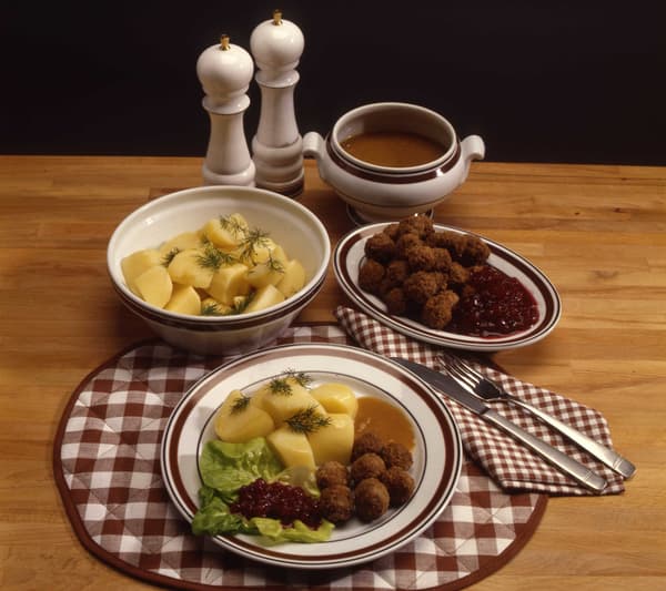 Köttbullar med tillbehör, upplagt på tallrikar och skålar på en rutig borsdtablett. 