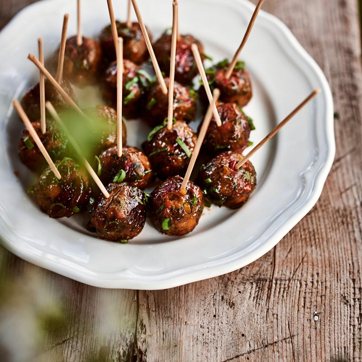 Köttbullar serverade med tandpetare ligger på en vit tallrik.