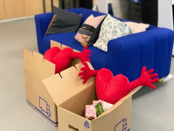 Krabice IKEA s červenými srdíčky a dalšími výrobky, za nimi stojí modré křeslo KLIPPAN.