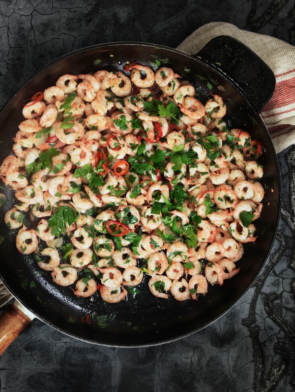 Krevety SJÖRAPPORT s petrželovou natí a chilli papričkami v litinové pánvi.