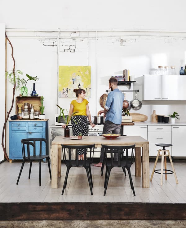 Kyra and Dave in their white kitchen with a wooden dining table and black chairs.