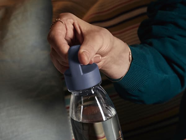 La main d’une personne portant un pull vert foncé, qui dévisse le bouchon d’une bouteille d’eau IKEA 365+ presque pleine.