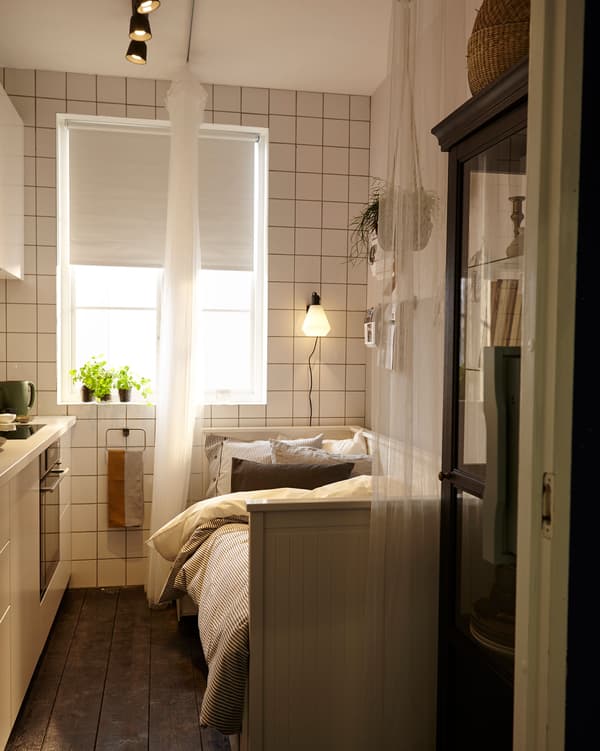 La même petite cuisine aménagée en chambre à coucher. Avec un convertible, un rideau fixé au plafond qui fait office de séparateur et une lampe de lecture au-dessus du lit.