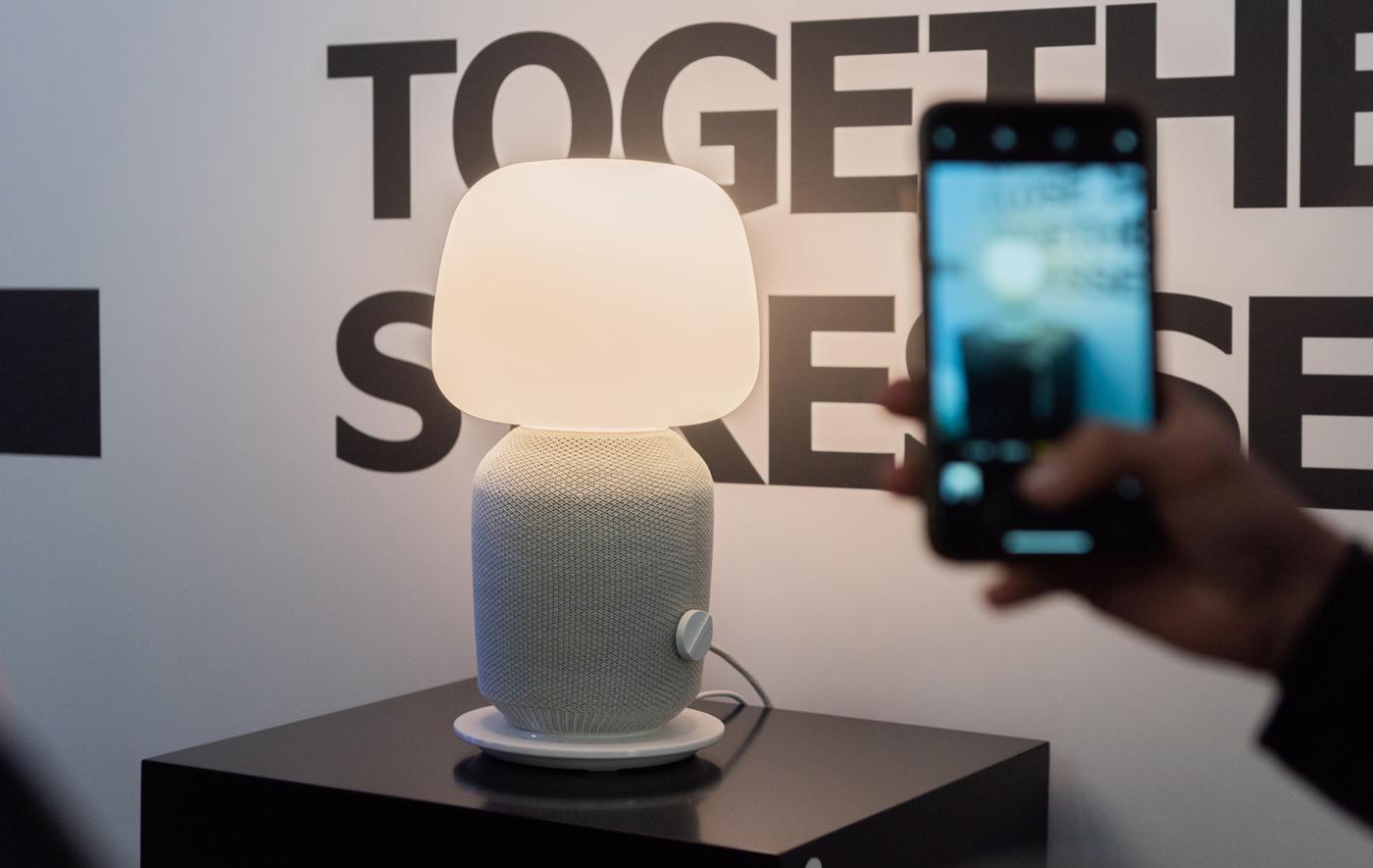La nouvelle enceinte SYMFONISK sous forme d'une lampe de table posée sur un meuble et photographiée à côté d’un texte.