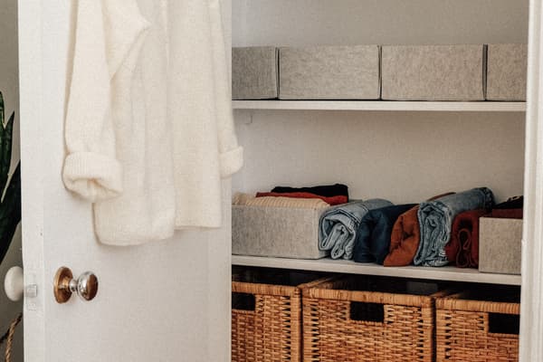 La porte du placard s’ouvre pour révéler les boîtes en feutre KOMPLEMENT en gris et les paniers BRANÄS en rotin.