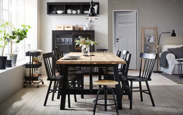 La table de salle à manger SKOGSTA en acacia est placée au centre d’une salle à manger beige et noire, entourée d’un mélange de chaises noires.