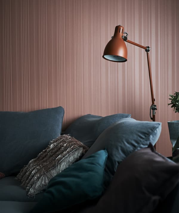 Lampadaire couleur rouille suspendu au-dessus d'un canapé gris installé contre un mur rouille.