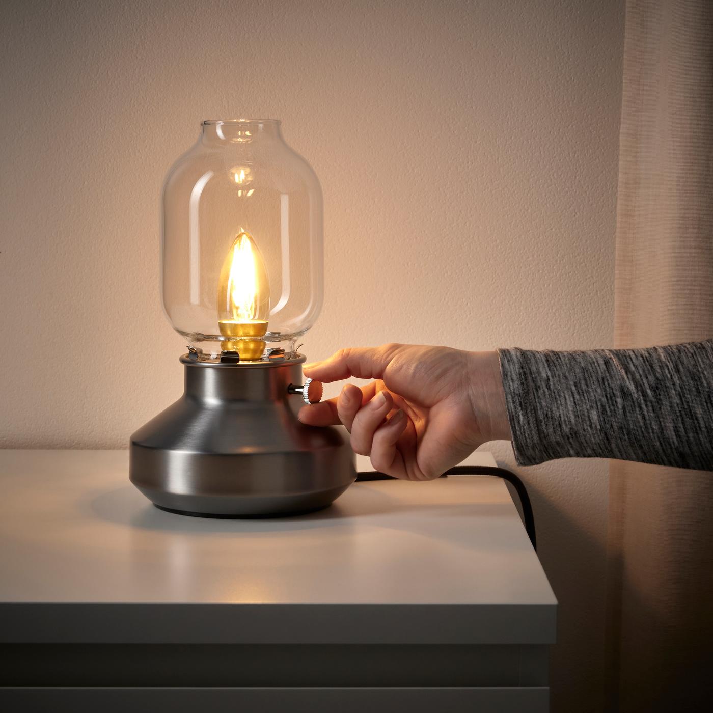 Lámpara de mesa TÄRNABY iluminando una mesa y una mano que la está prendiendo.