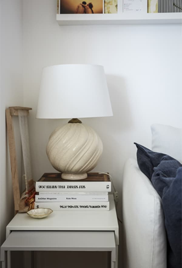 Lampe blanche posée sur une pile de livres, sur des tables gigognes.