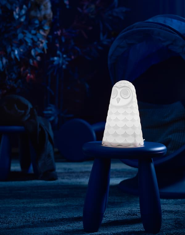 Lampe de table pour enfants SOLBO à DEL blanche en forme de hibou posée sur un tabouret en plastique dans une aire de jeu sombre.