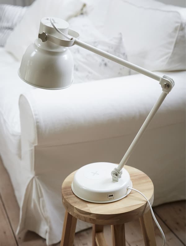 Lampe sur un tabouret en bois, à côté d’un canapé blanc.