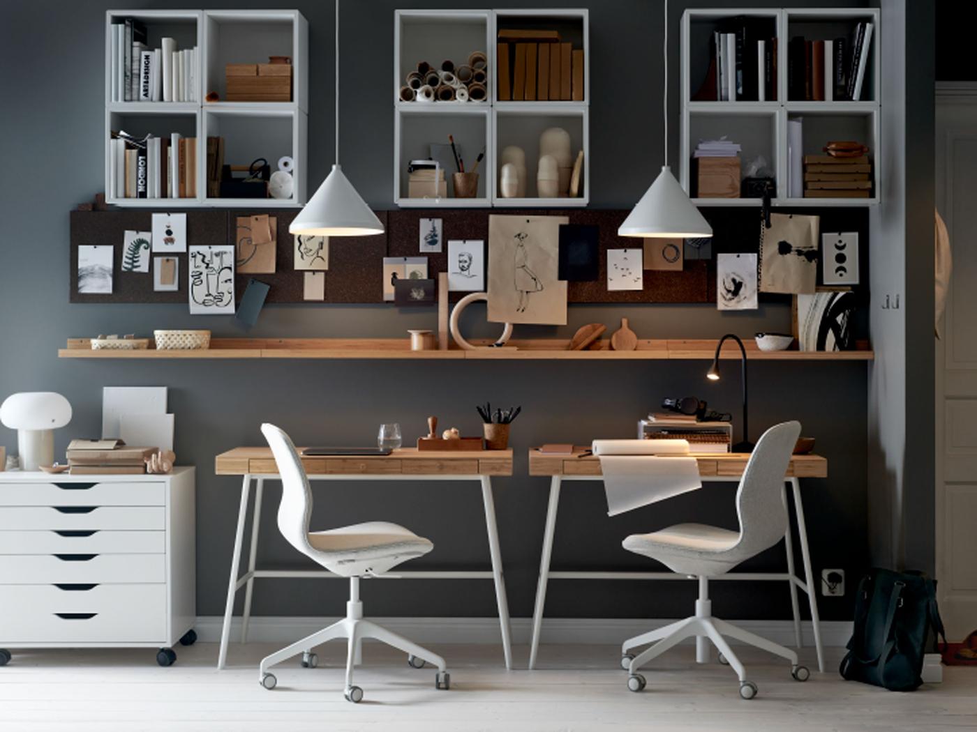 חלל עבודה עם שני כיסאות משרדיים LÅNGFJÄLL ליד שולחנות כתיבה LILLÅSEN, עם מדפים, לוחות מודעות ומנורות תלייה לבנות.
