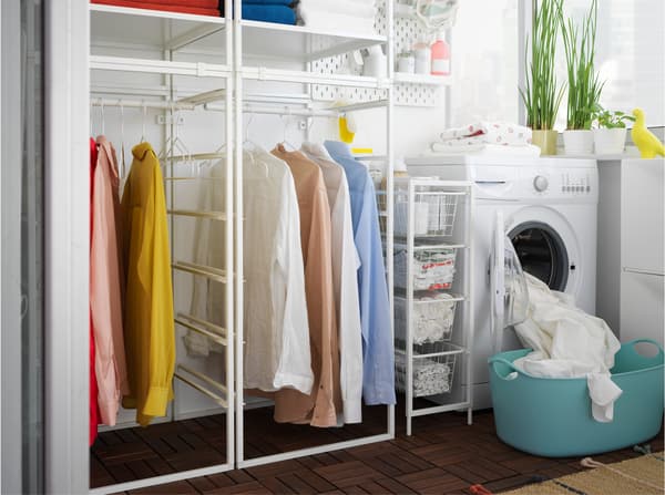 Laundry room with JONAXEL white shelving unit, clothes on the rail and a washing machine and laundry basket beside.