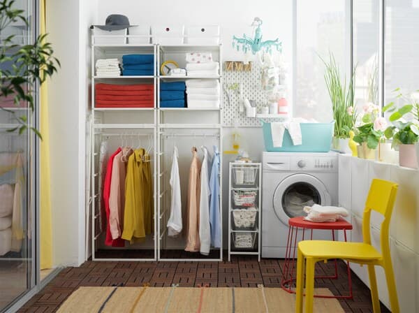 Laundry room with JONAXEL white shelving unit, towels on the shelves, clothes on the rail and a washing machine beside.