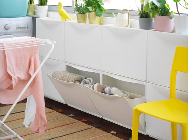 Laundry room with open TRONES white shoe cabinet, displaying shoes and clothing, plus drying laundry hanging on a white frame.