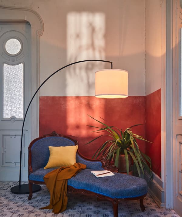Le coin d’une pièce avec des articles raffinés et des détails. Un lampadaire SKAFTET éclaire une grande plante et un divan élégant.