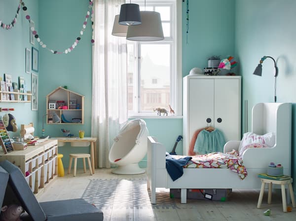 Le lit extensible et l'armoire IKEA BUSUNGE blancs et la table pour enfant FLISAT en bois clair peuvent transformer la pièce en salle de jeux, en bougeant des pièces en toute sécurité.